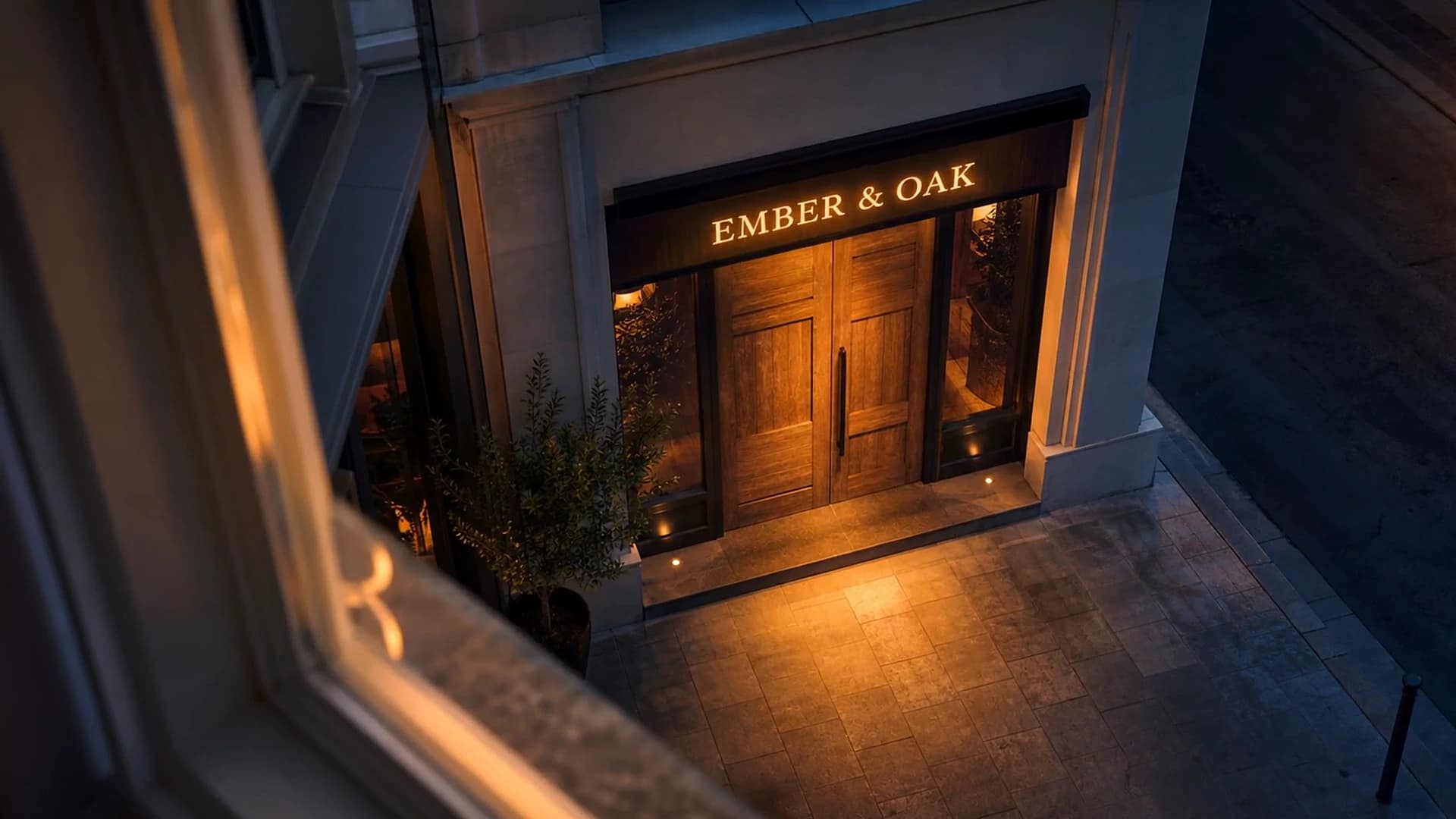Looking down through the office window at dusk: the warm Ember & Oak sign glows over the door.
